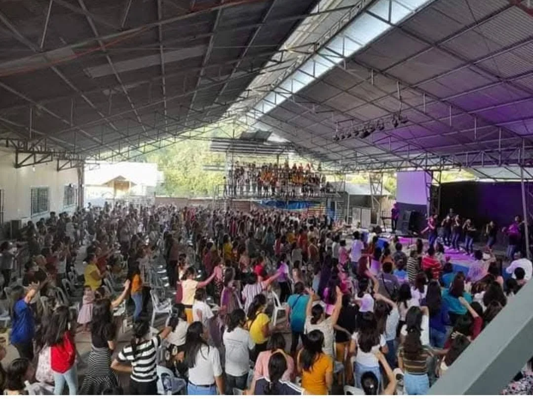 A congregation worshipping together at a revival gathering in a covered hall